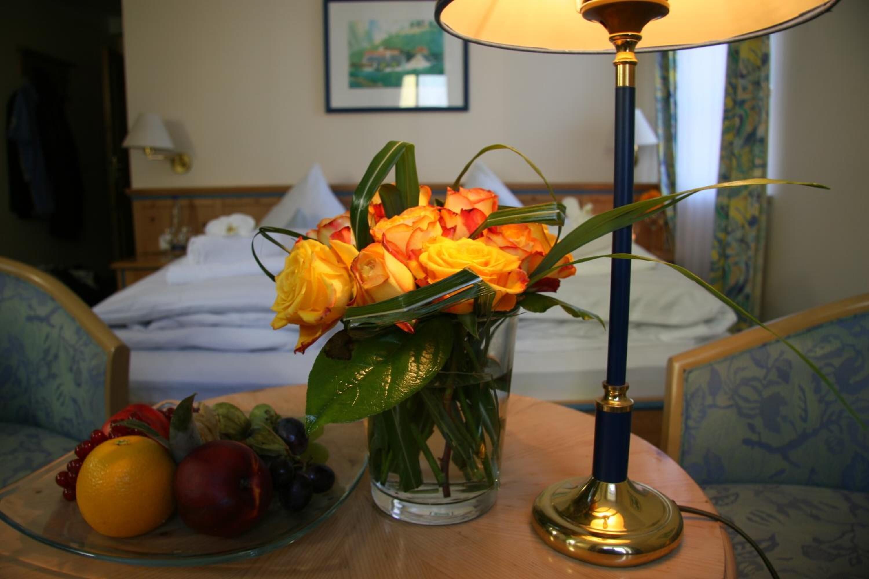 Ein Zimmer mit einem Bett, einem Nachttisch mit Lampe, einer Blumenvase und einer Obstschale.