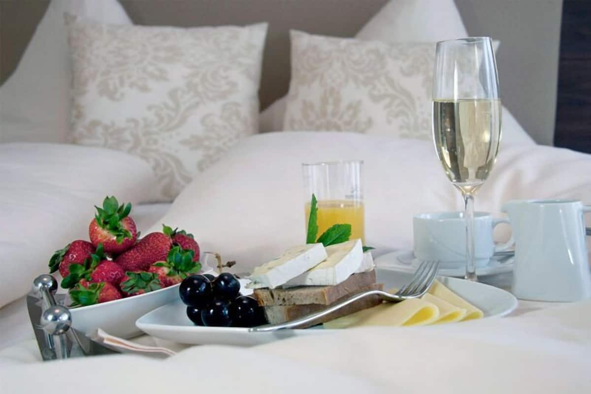 Une table de petit-déjeuner joliment dressée, avec des fraises, des raisins, du fromage et un verre de jus, posée sur une table recouverte d’une nappe blanche et agrémentée d’oreillers à motifs.