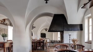 A spacious dining area with high ceilings and arched alcoves, featuring a large black chandelier and a stone fireplace. - Zamek Zabreh (Ostrava)