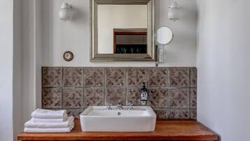 Ein Badezimmer mit einem Holzbadezimmerhocker, einem weißen Waschbecken, einem Spiegel und einem an der Wand befestigten Handtuchhalter.