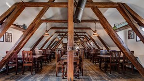 A spacious attic dining area with wooden beams, tables, and chairs arranged for dining. - Zamek Zabreh (Ostrava)