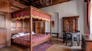 A four-poster bed with a red and gold canopy, a wooden desk with chairs, and a large mirror with ornate woodwork. - Zamek Zabreh (Ostrava)