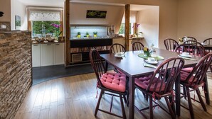 Un área de comedor con una mesa de madera y sillas acolchadas, una cocina al fondo y una pared de piedra en un lateral.