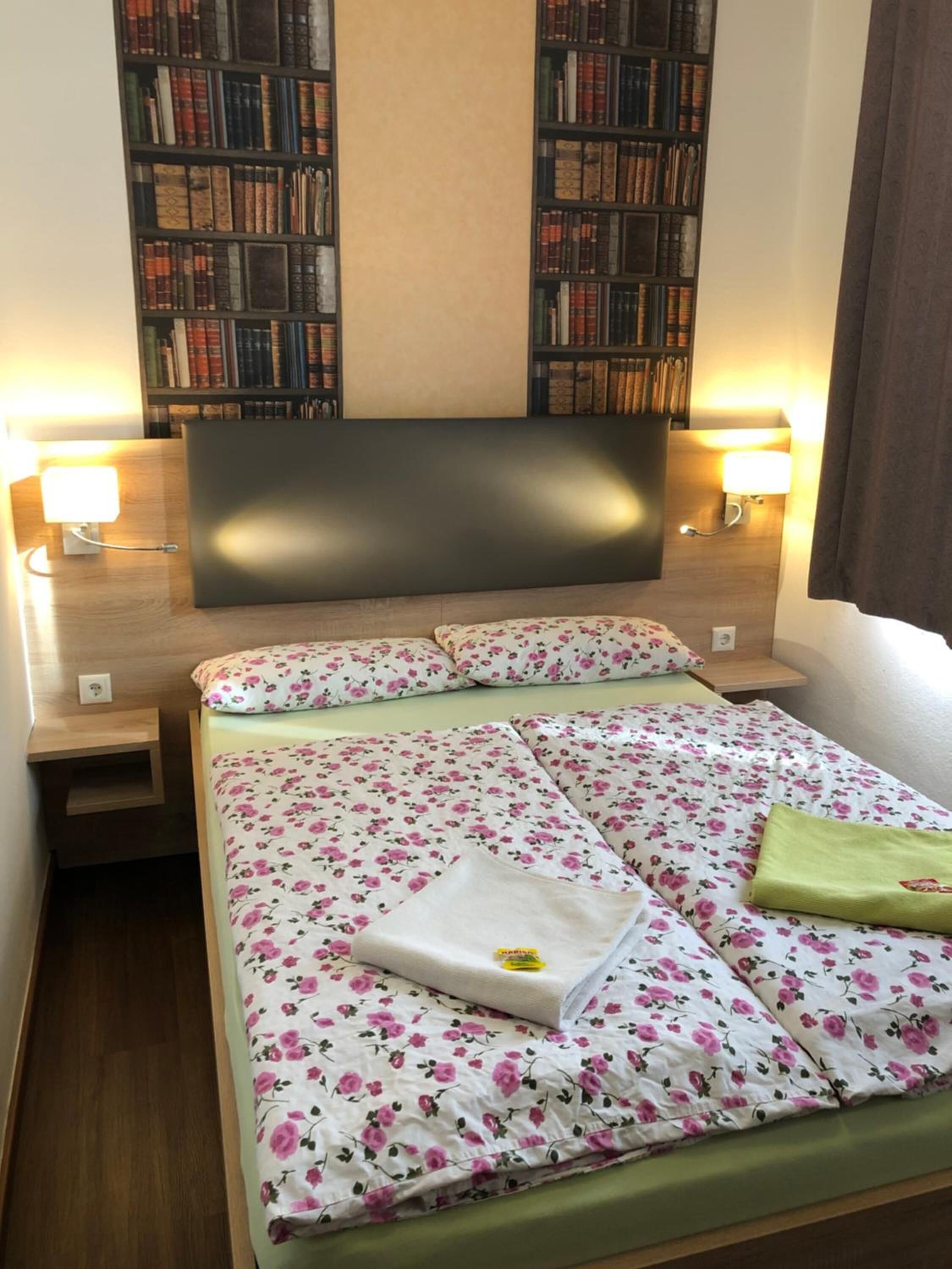 Et hotelværelse med en seng, to sengeborde, et natbord, en reol og en sengegavl.
