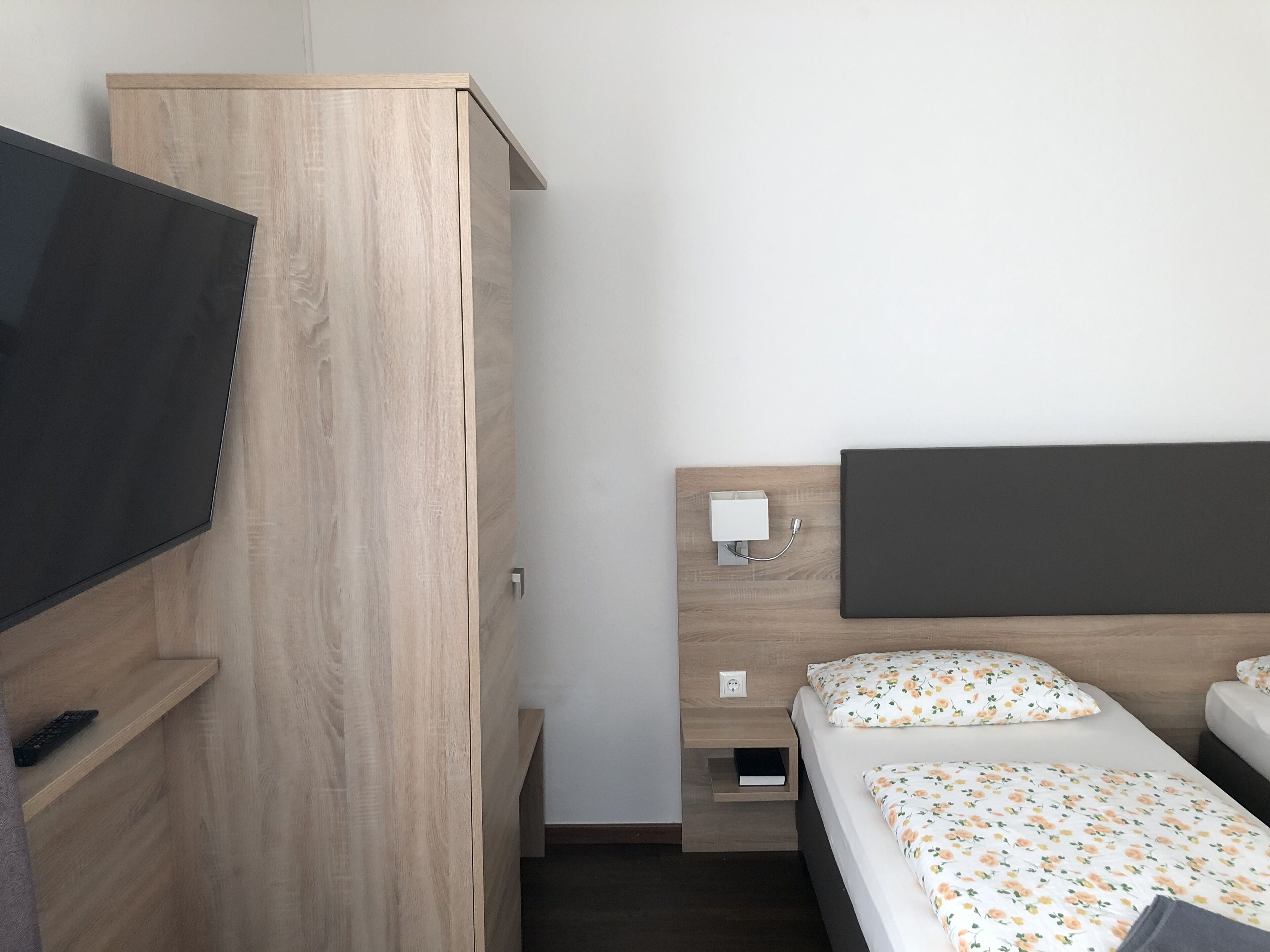 Una habitación de hotel con un armario de madera, una cama con ropa de cama floral, una mesita de noche con una lámpara y un televisor a la izquierda.