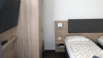 Una habitación de hotel con un armario de madera, una cama con ropa de cama floral, una mesita de noche con una lámpara y un televisor a la izquierda.