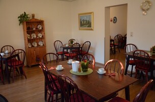 Un comedor con mesas y sillas de madera, una estantería con platos y un cuadro en la pared.
