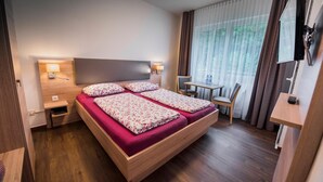 Habitación de hotel con cama doble, dos mesitas de noche, un escritorio, una silla y televisor.