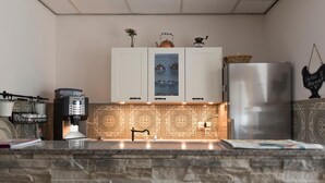 Una cocina con armarios blancos, una cafetera, un hervidor y un refrigerador.