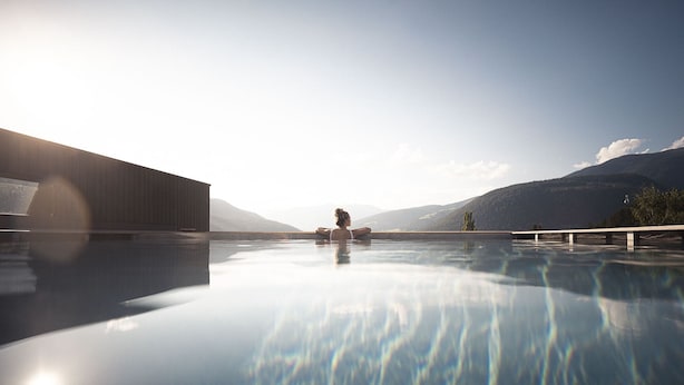 Un espace piscine extérieur paisible, offrant une vue dégagée sur les montagnes lointaines, avec un bâtiment en bois et une personne se relaxant au bord de la piscine.