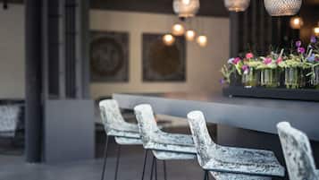 Een moderne bar met drie witte barstoelen, een donkere bar en decoratieve hanglampen.