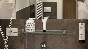 A bathroom with a white sink, a mirror, a towel rack, a glass soap dispenser, and a hairdryer on the wall.