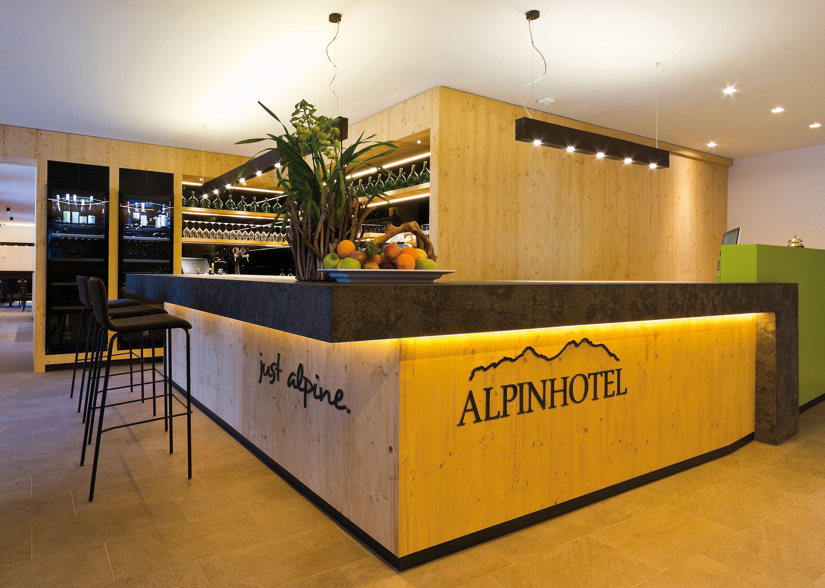 Un comptoir d’accueil avec un revêtement en bois, des tabourets de bar et un présentoir de fruits.