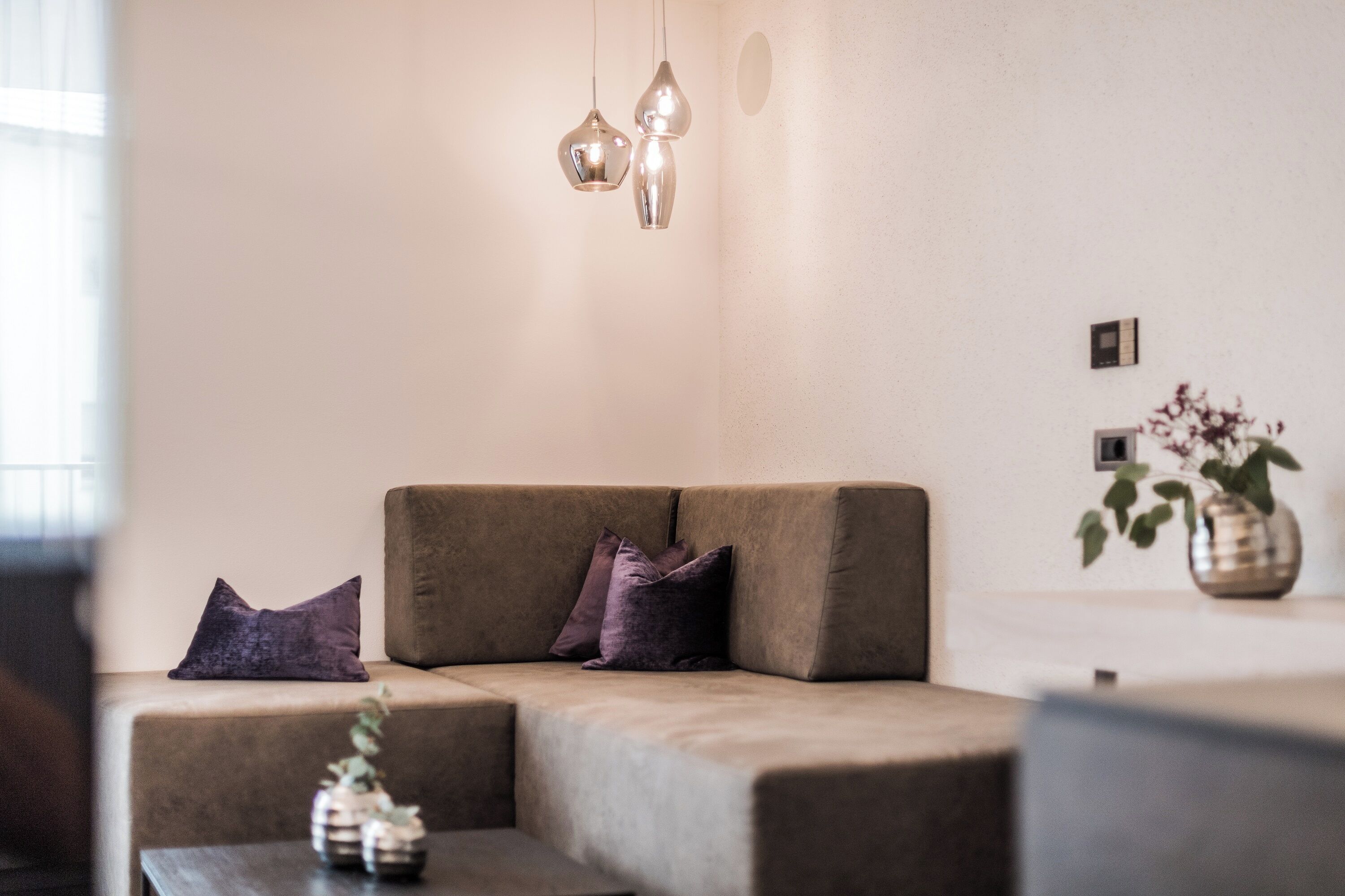 Un salon moderne avec un canapé d’angle, deux lampes suspendues et une petite table agrémentée d’objets décoratifs.