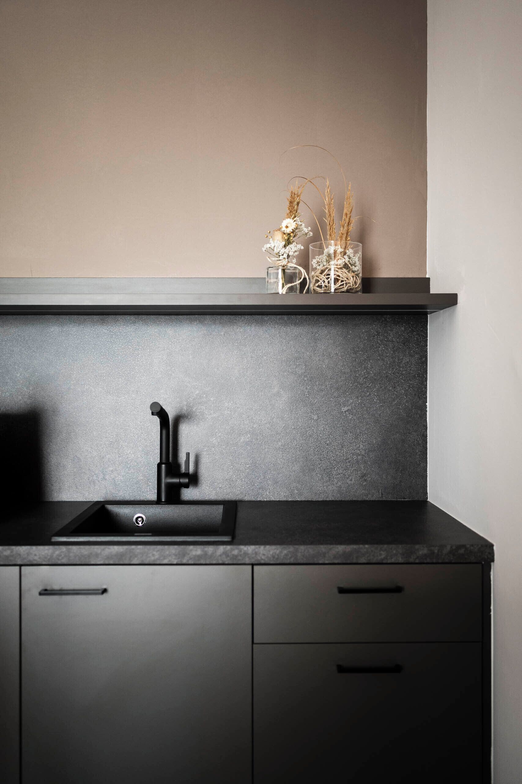 A modern kitchen with a black countertop, a sink, and a shelf above it.