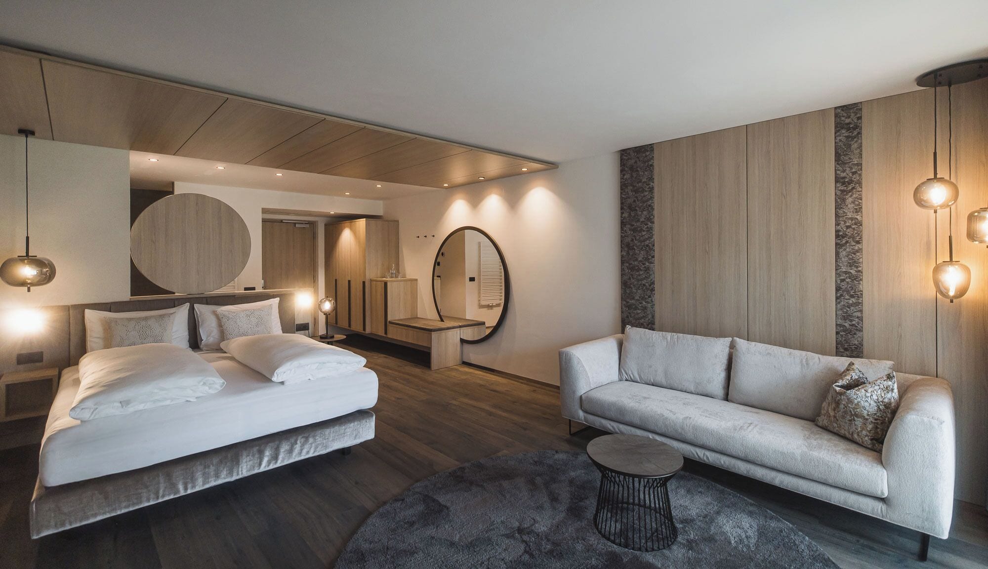 A modern bedroom with a bed, a sofa, a round mirror, and a small table.