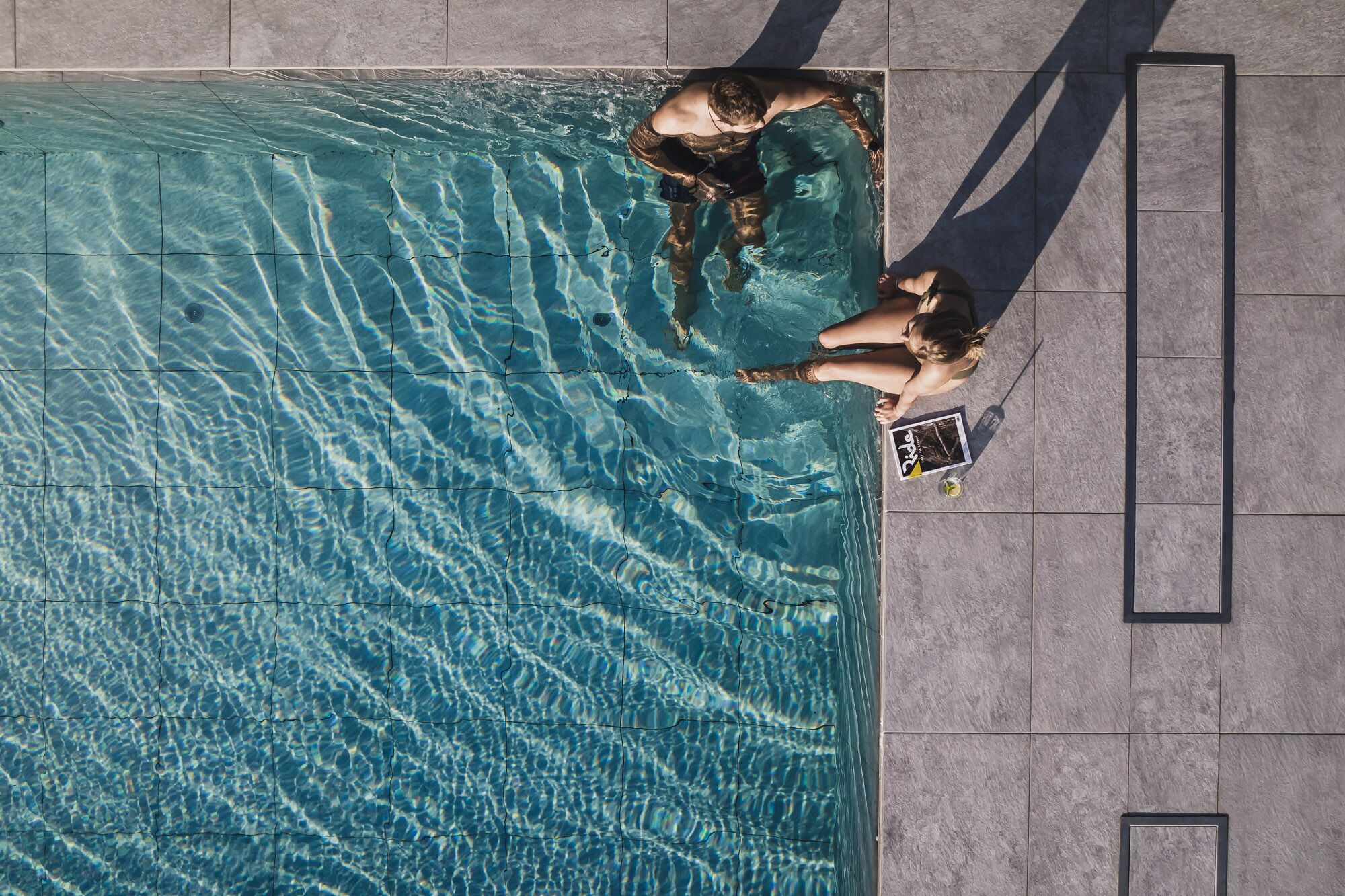 An aerial view of a swimming pool with clear water, surrounded by tiled flooring.