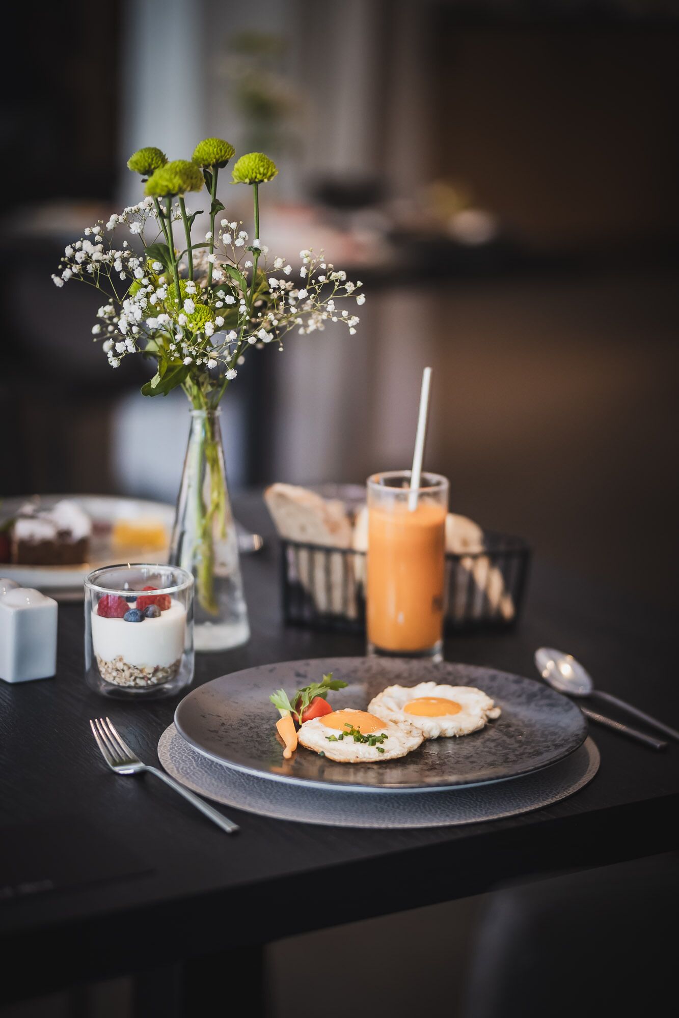 Een eettafel met een bord eten, een glas smoothie en een bloevas.