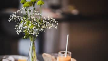 Een eettafel met een bord eten, een glas smoothie en een bloevas.