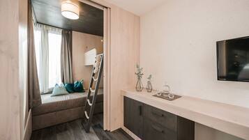Una habitación de hotel moderna con un banco de madera junto a la ventana, una mesita con objetos decorativos y un televisor montado en la pared.