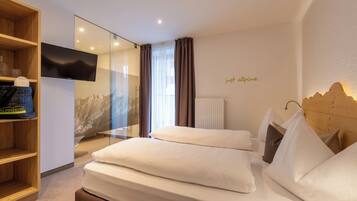 Habitación de hotel moderna con una cama grande, un televisor, un estante de madera con objetos y vistas a la montaña.