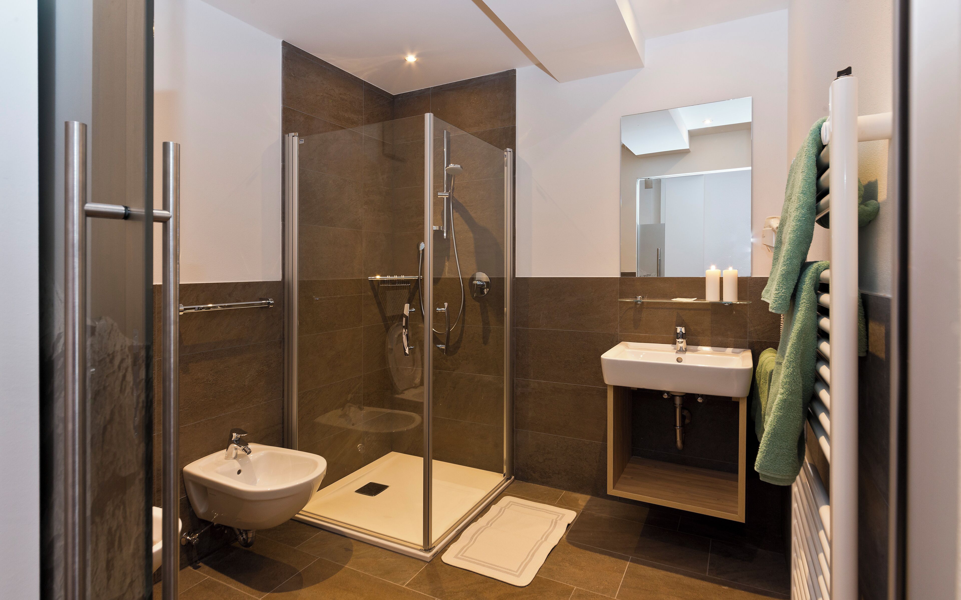 Un baño moderno con ducha envuelta en vidrio, lavamanos pedestal y tocador con espejo.