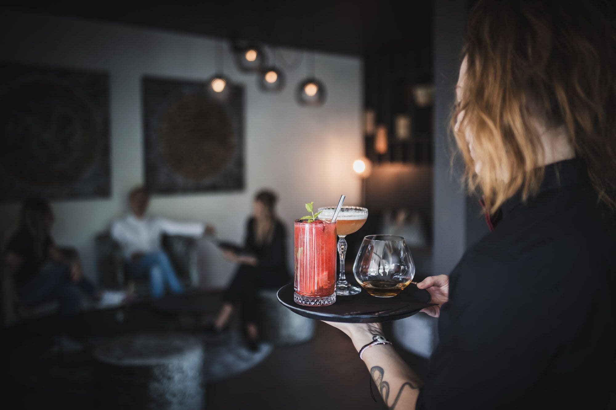 A person holding a tray with a cocktail, a glass of beer, and a margarita.