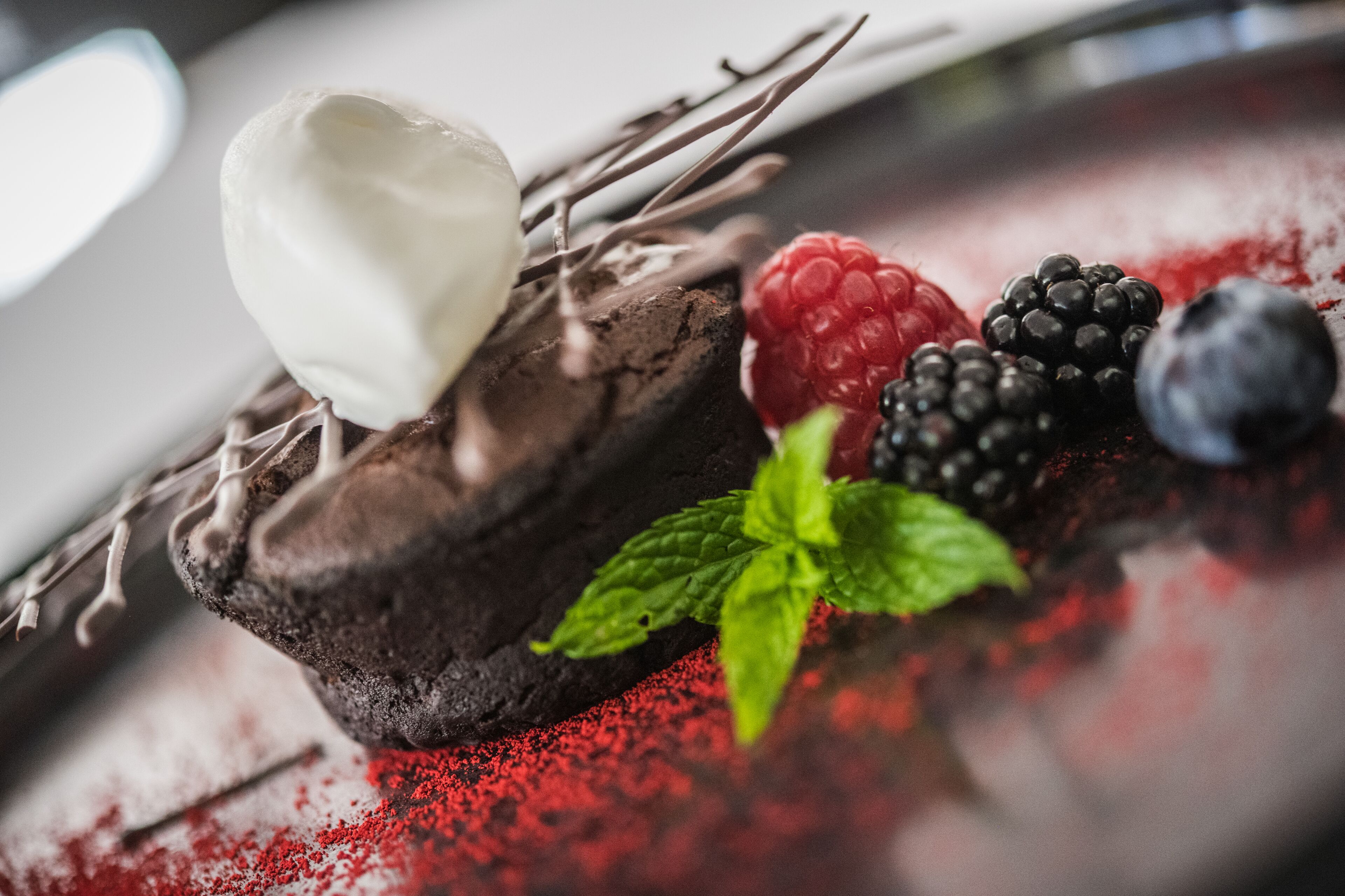 A dessert with chocolate cake, whipped cream, berries, and mint leaves.