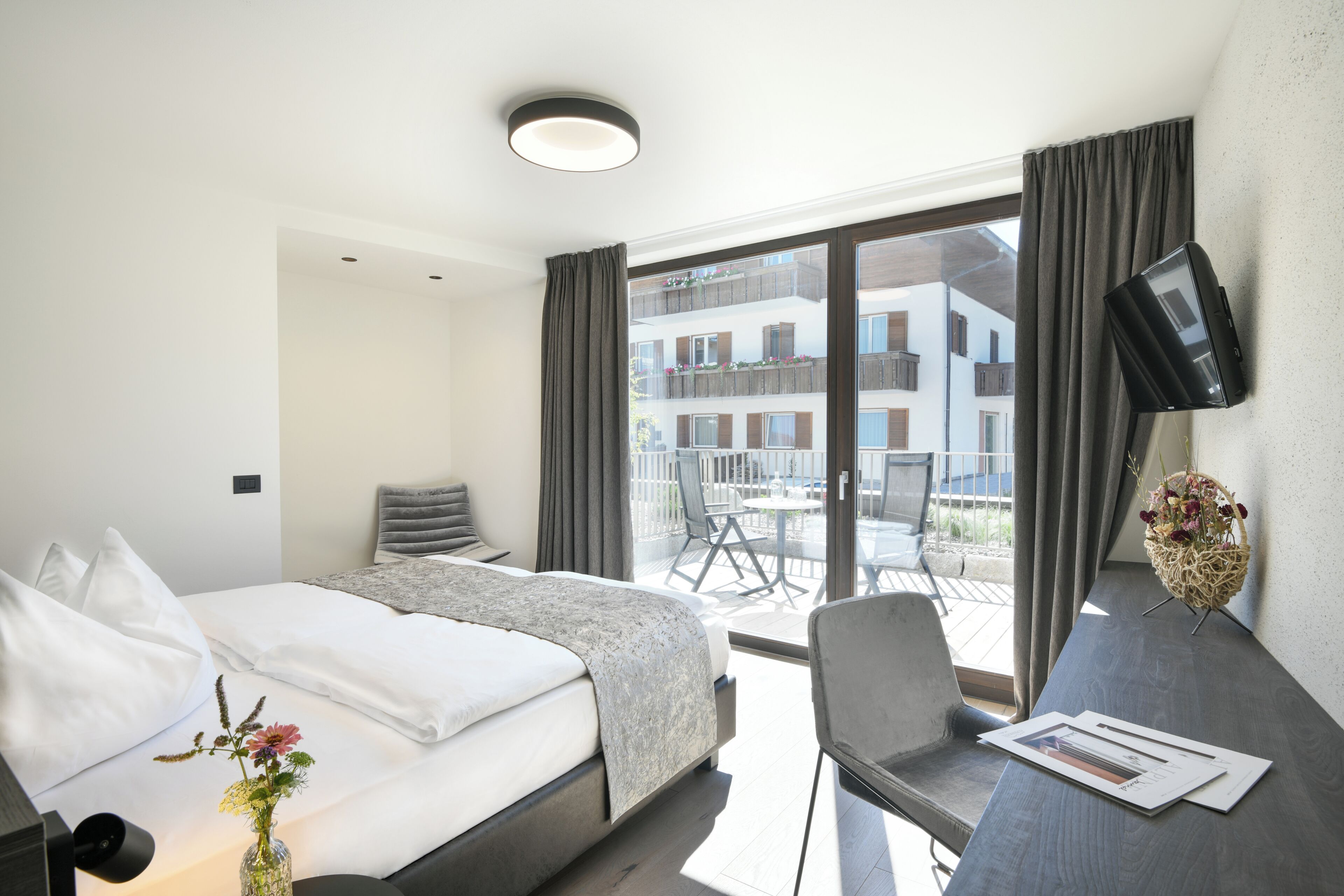 Een hotelkamer met een bed, een bureau, een televisie en een balkon met uitzicht op gebouwen.