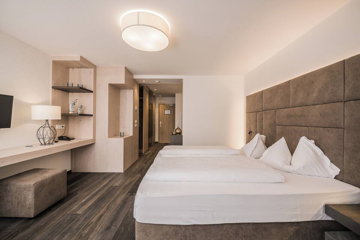 A hotel room with a large bed, a desk with a lamp, and a TV on the wall.