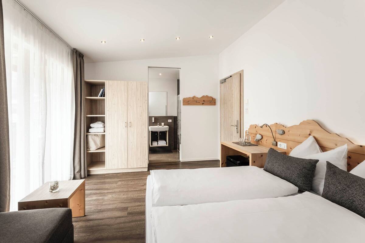 A hotel room with a bed, a desk, a wardrobe, and a bathroom visible through an open door.