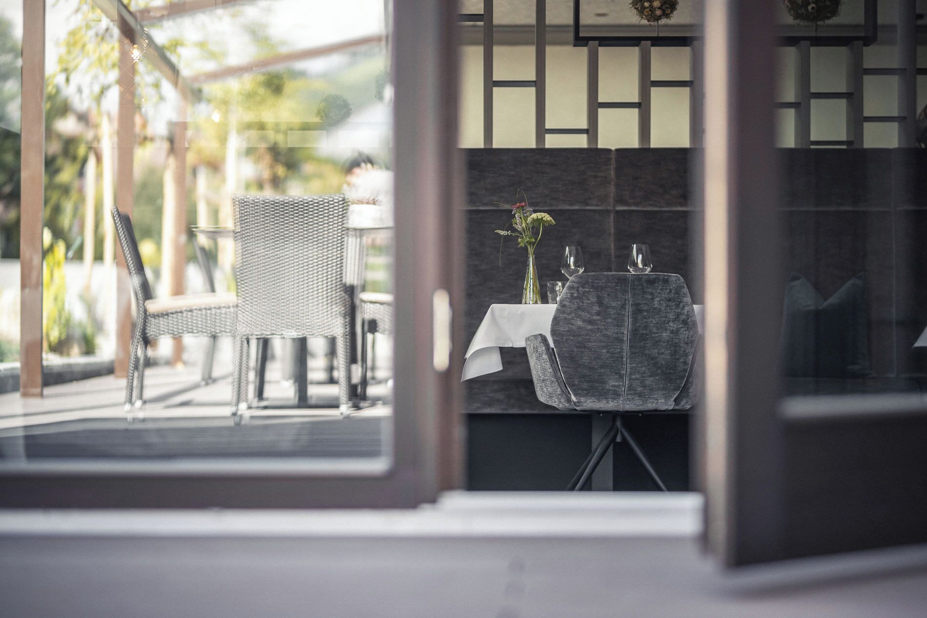An outdoor dining area with wicker chairs and a table set for two, featuring a vase with flowers.