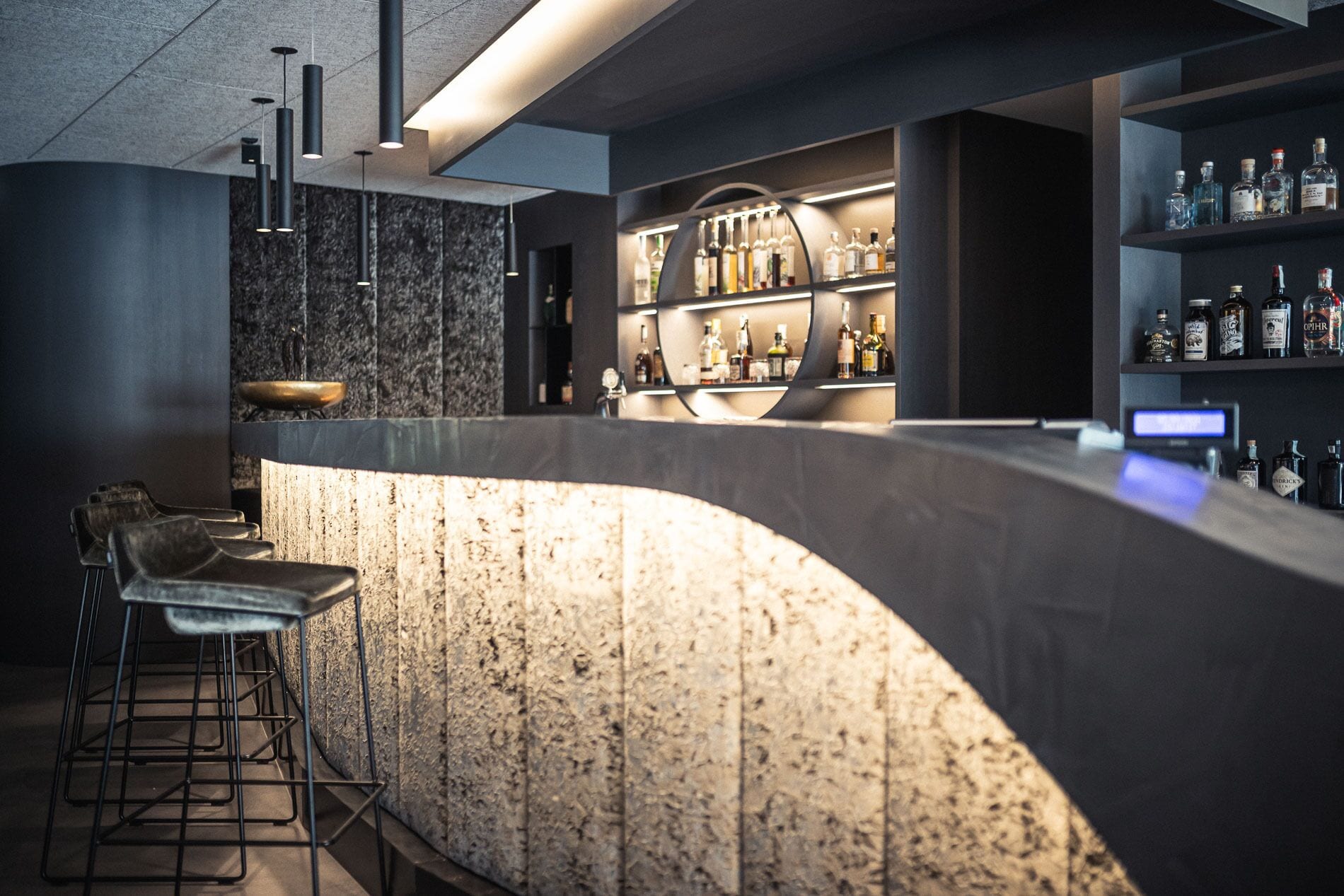 Eine moderne Bar mit einer gebogenen Theke, Barhocker und Regalen voller Flaschen.