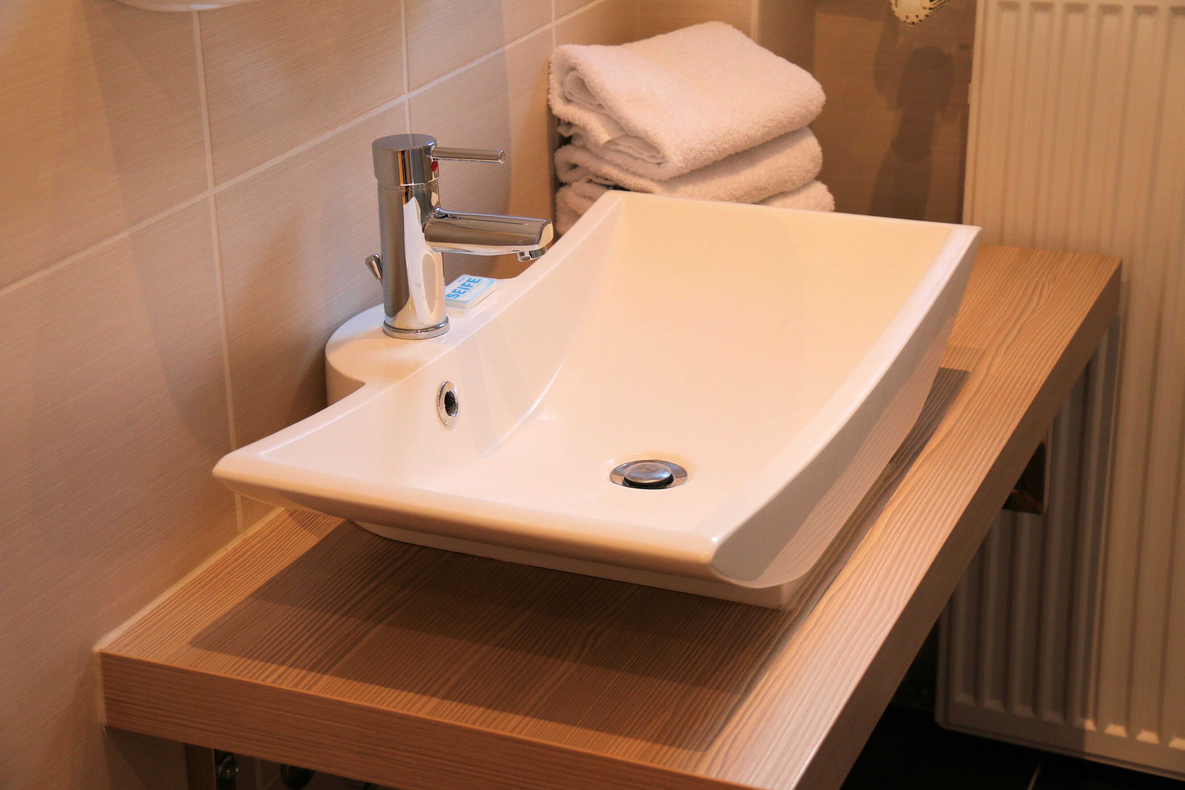 Une salle de bain avec un lavabo blanc, un plan de toilette en bois et des serviettes pliées.