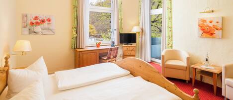 A hotel room with a large bed, a desk with a chair, a TV, and a small table with a chair.