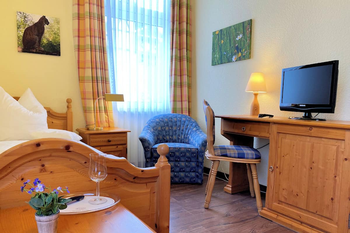 Une pièce confortable avec un lit, un bureau doté d’une télévision, une chaise, une lampe et une fenêtre avec des rideaux.