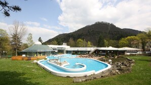 Une piscine au design original, entourée d’une pelouse et avec une montagne en toile de fond.