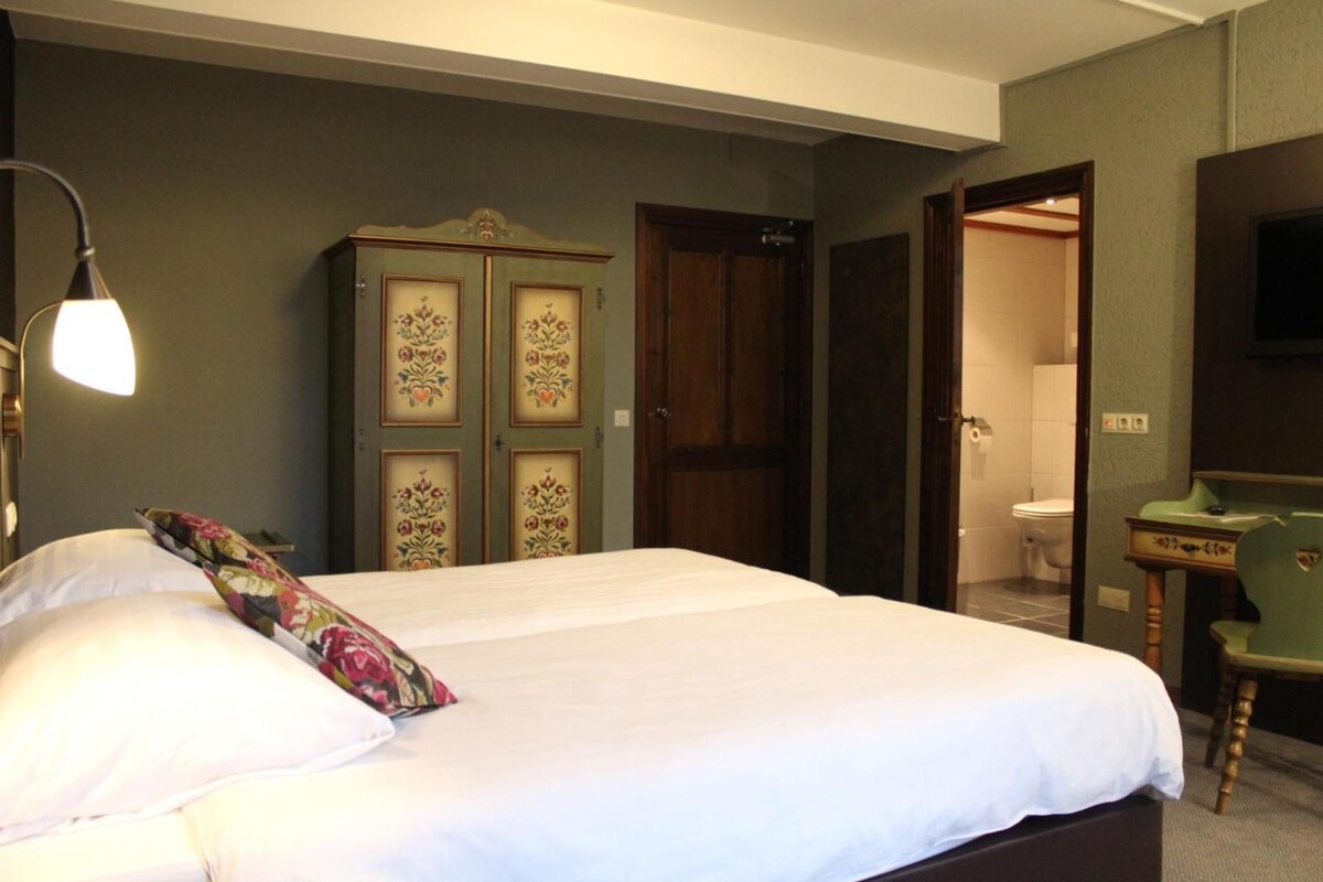 A hotel room with a bed, a desk, a mirror, and a wardrobe.