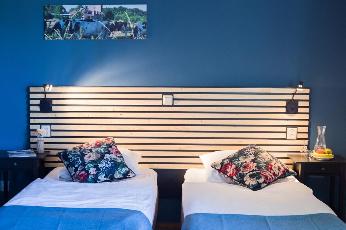 A double bed with a wooden headboard, two pillows, a bedside table with a lamp, and a wall-mounted picture.