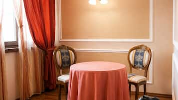 Une pièce avec une table ronde recouverte d’une nappe rose, deux chaises à l’assise à motifs, un luminaire fixé au mur et une petite table sur laquelle se trouvent une bouilloire et des tasses.