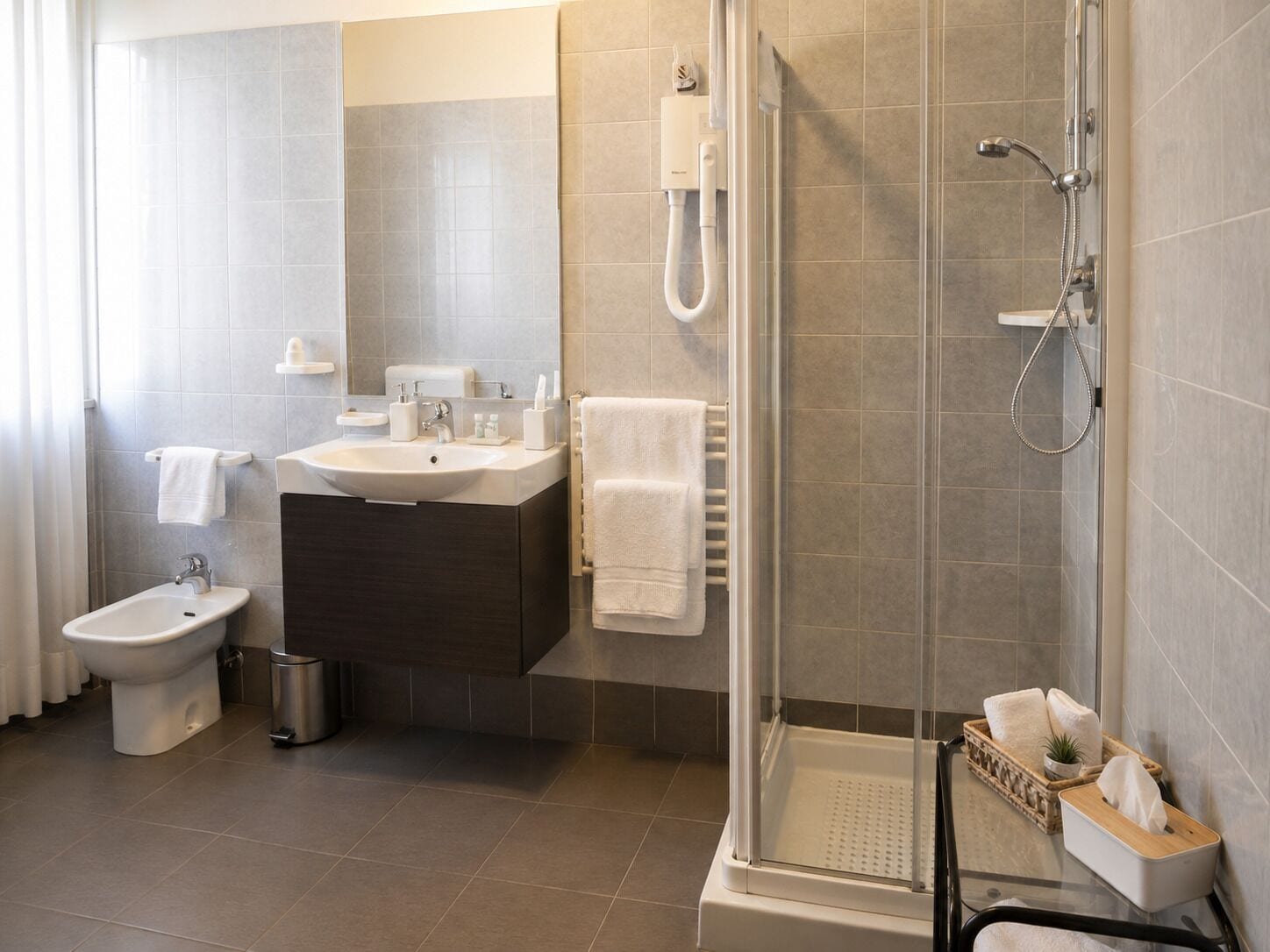 Une salle de bain moderne équipée d’une douche, de toilettes, d’un bidet et d’un meuble-lavabo avec un évier et un porte-serviettes.