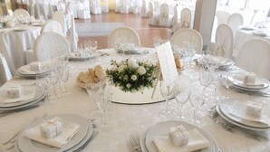 A banquet hall with round tables set for a formal event, complete with place settings, wine glasses, and floral centerpieces.