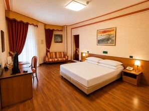 Une chambre d’hôtel avec un lit, un bureau, une chaise, un canapé et un tableau au mur.