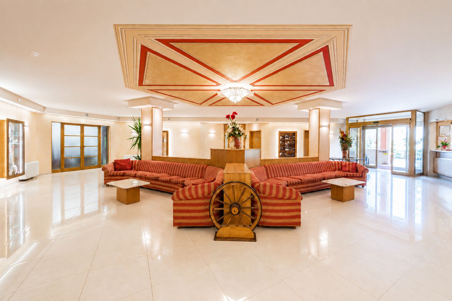 Un hall d’entrée spacieux, doté d’un grand canapé d’angle, d’une roue en bois décorative et d’un plafond haut orné de motifs géométriques.