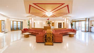 Un hall d’entrée spacieux, doté d’un grand canapé d’angle, d’une roue en bois décorative et d’un plafond haut orné de motifs géométriques.