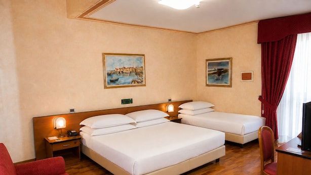 A hotel room with a large bed, a smaller bed, a desk with a chair, and two paintings on the wall.