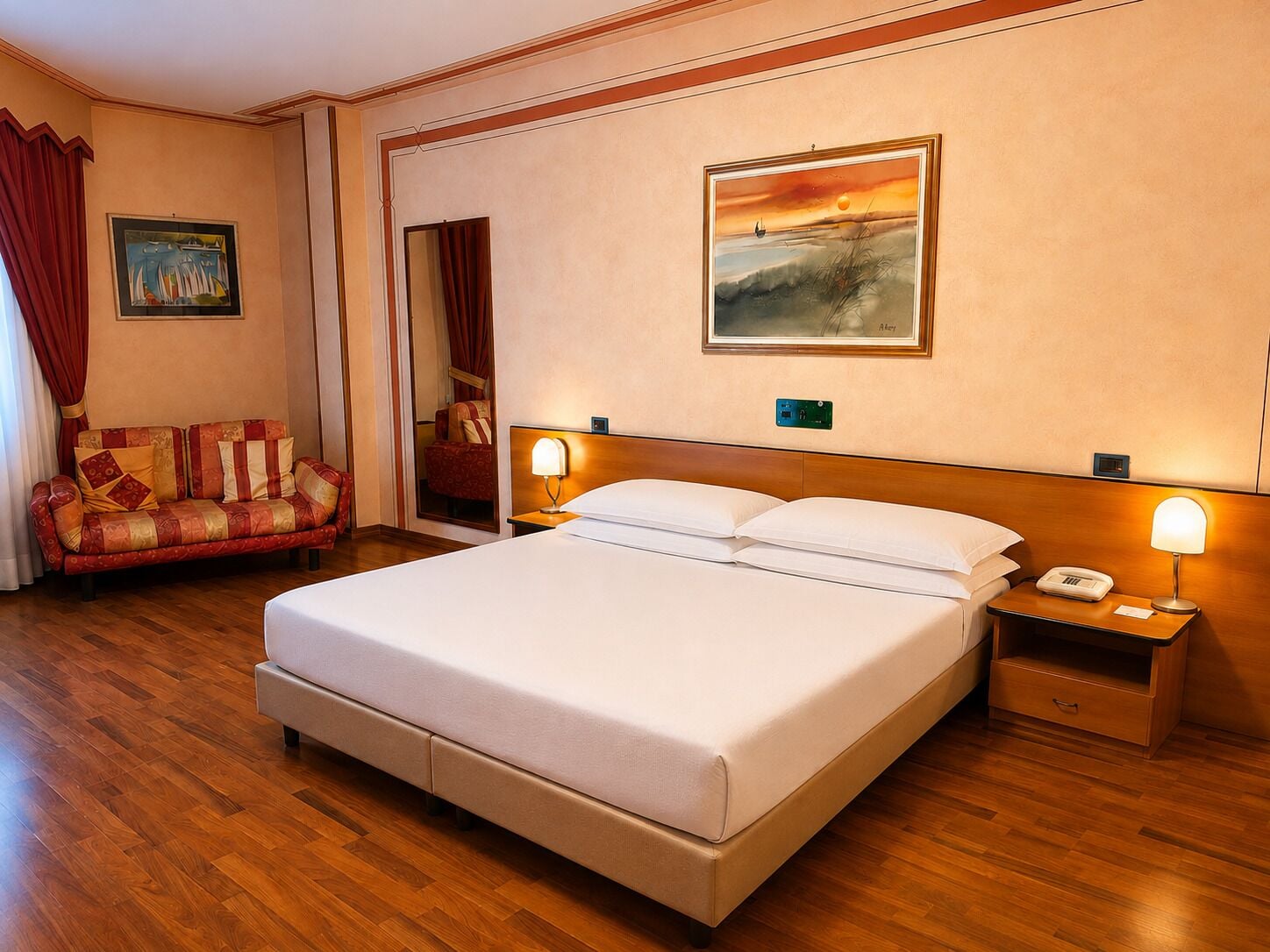 A hotel room with a bed, a nightstand, a lamp, a painting, a sofa, and a window with curtains.