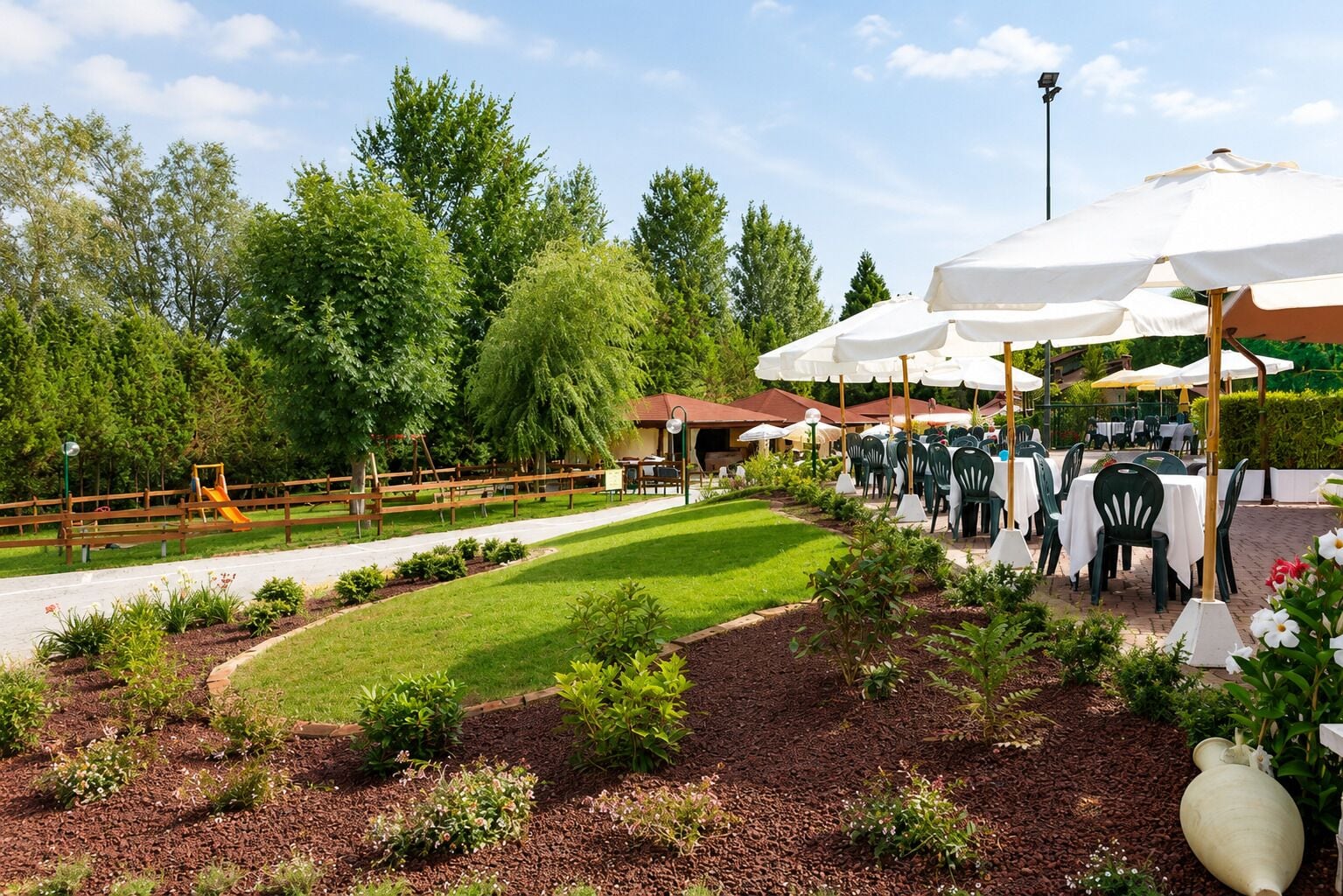 An outdoor dining area with tables and chairs, surrounded by greenery and trees.