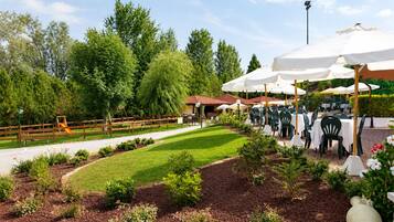 An outdoor dining area with tables and chairs, surrounded by greenery and trees.
