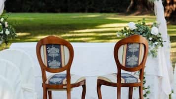 Ein Hochzeitbogen mit floralen Dekorationen und zwei hölzerne Stühle mit gepolsterten Sitzflächen.